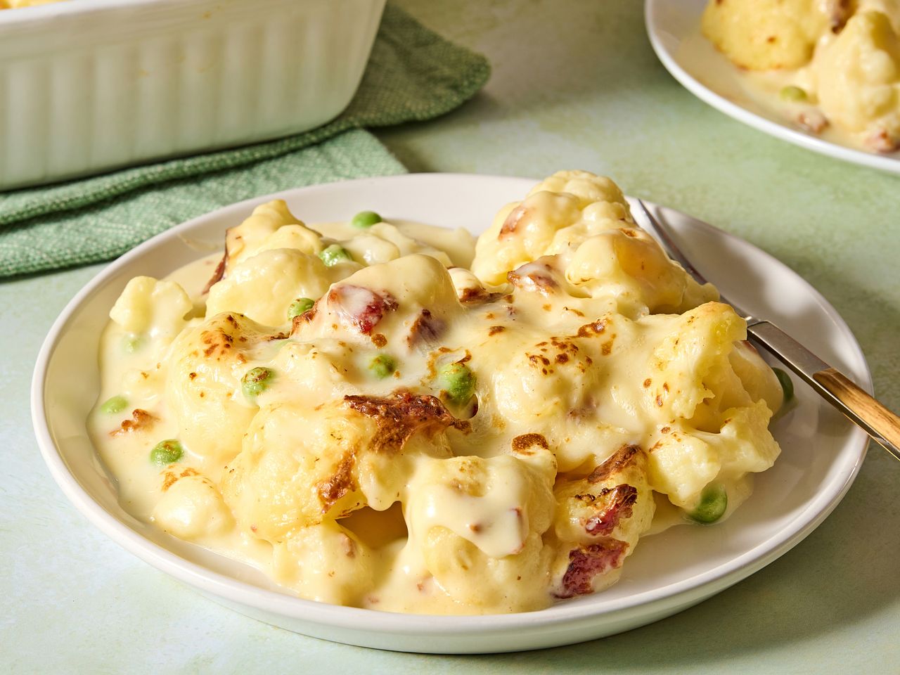 Plate of cauliflower alfredo bake with peas and a fork