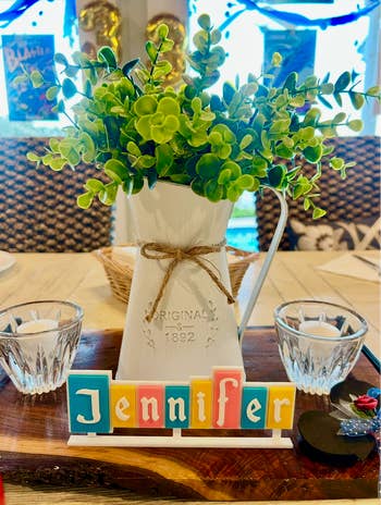 Vase with leafy plant, two candles, on wooden tray. Colorful blocks spell