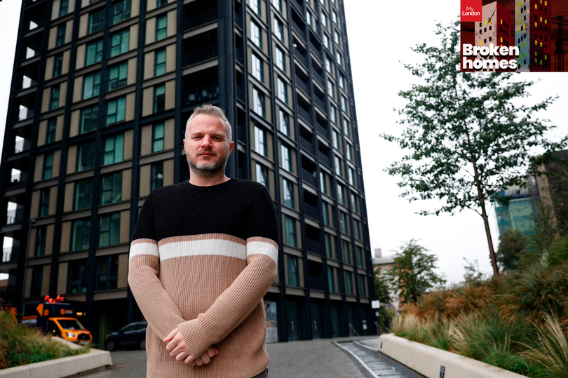 A man in a beige and black jumped with a white stripe standing in front of a black clad tower block