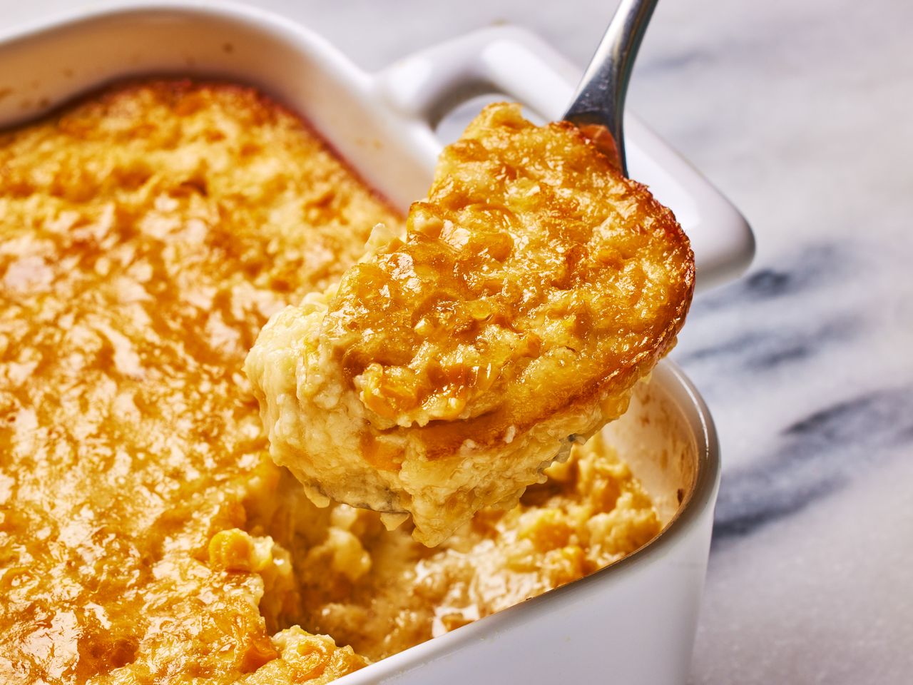 A baking dish of Grandma's corn pudding, with a spoonful of corn pudding