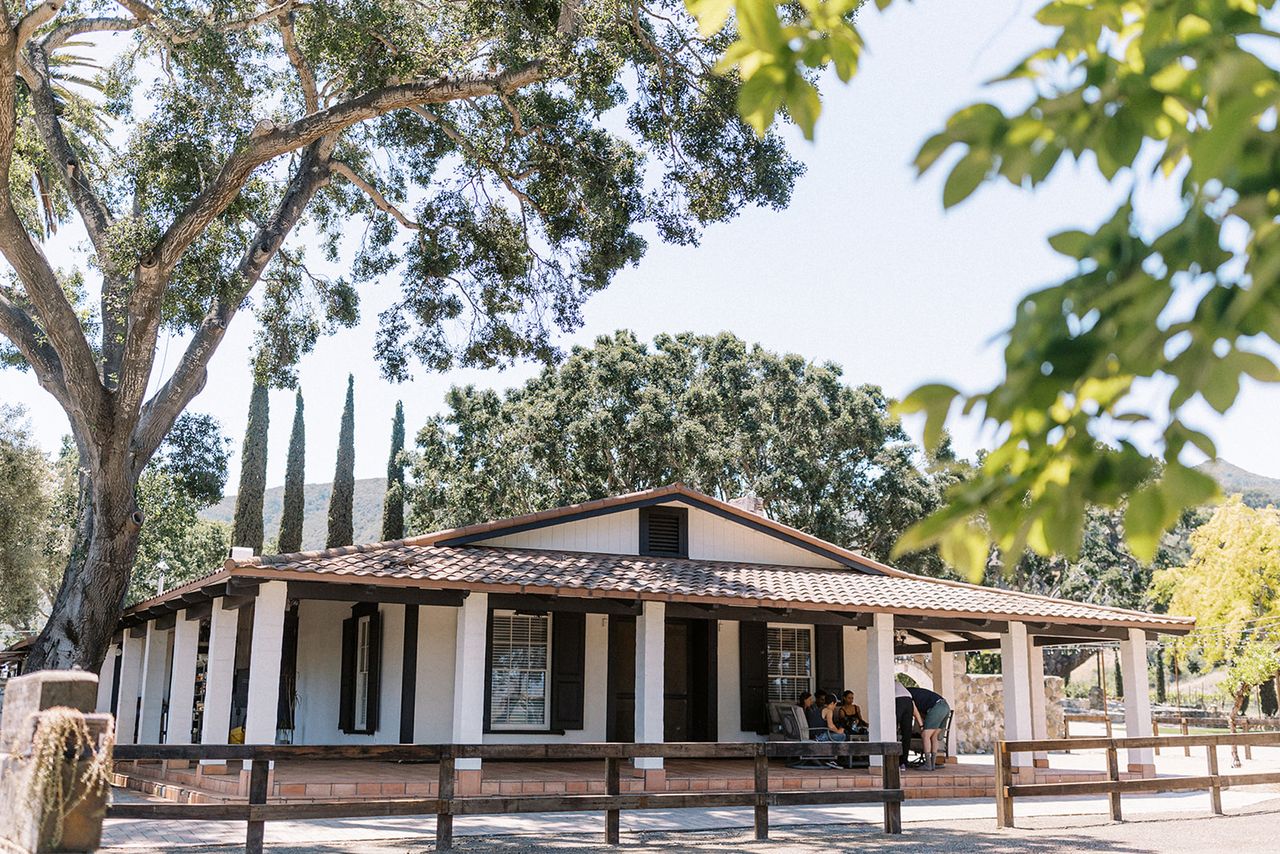 A singlestory building with a porch surrounded by large trees in a sunny environment