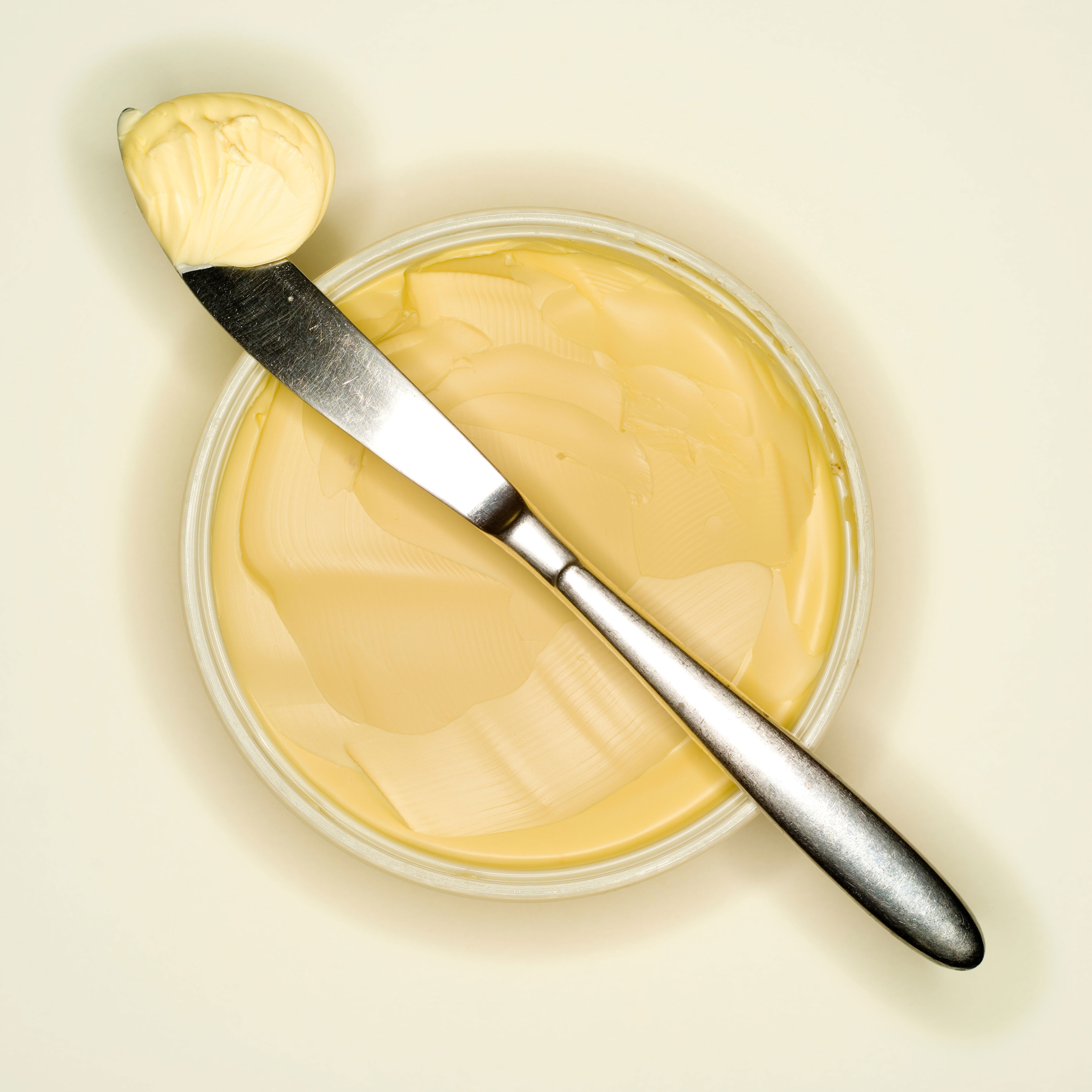 Butter in a round container with a spreading knife resting on top, holding a dollop