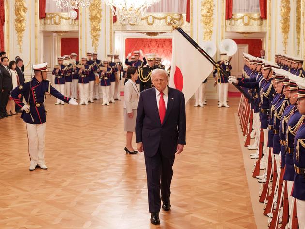 Da weicht er plötzlich von ihrer Seite: Während Sanae Takaichi vor den Fahnen innehält, schreitet Donald Trump weiter die Reihe der Uniformierten ab.