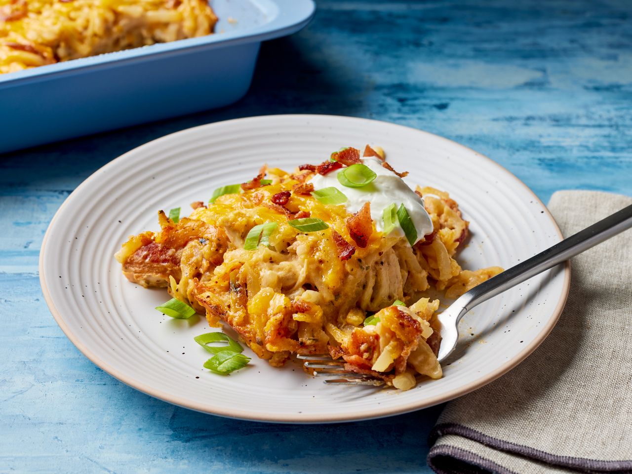 Loaded Chicken and Hash Brown Casserole on a plate with sour cream and green onions on a plate with a fork