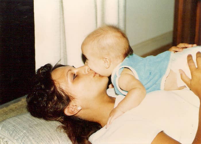 A woman lies on a couch as a baby playfully leans on her, gently touching her face with their nose. They both appear relaxed and content