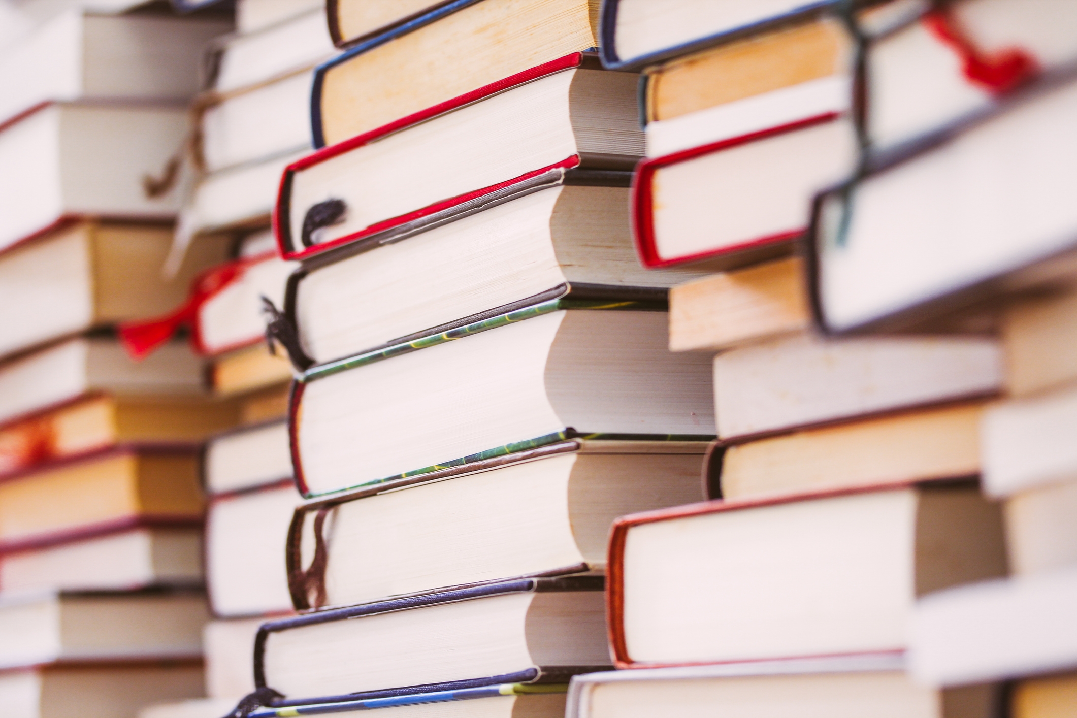 Stacks of books piled closely together, showing numerous covers and pages