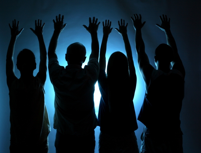 Silhouettes of four people raising their arms above their heads with bright light behind them, creating a dramatic effect