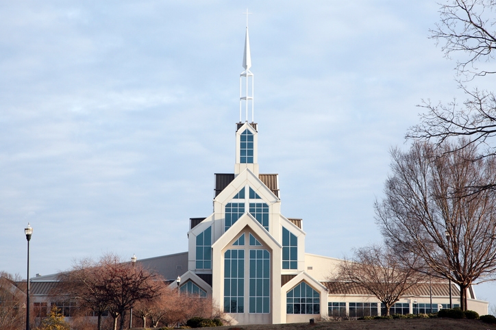 A modern church building with a prominent spire and large geometric windows, surrounded by leafless trees under a cloudy sky