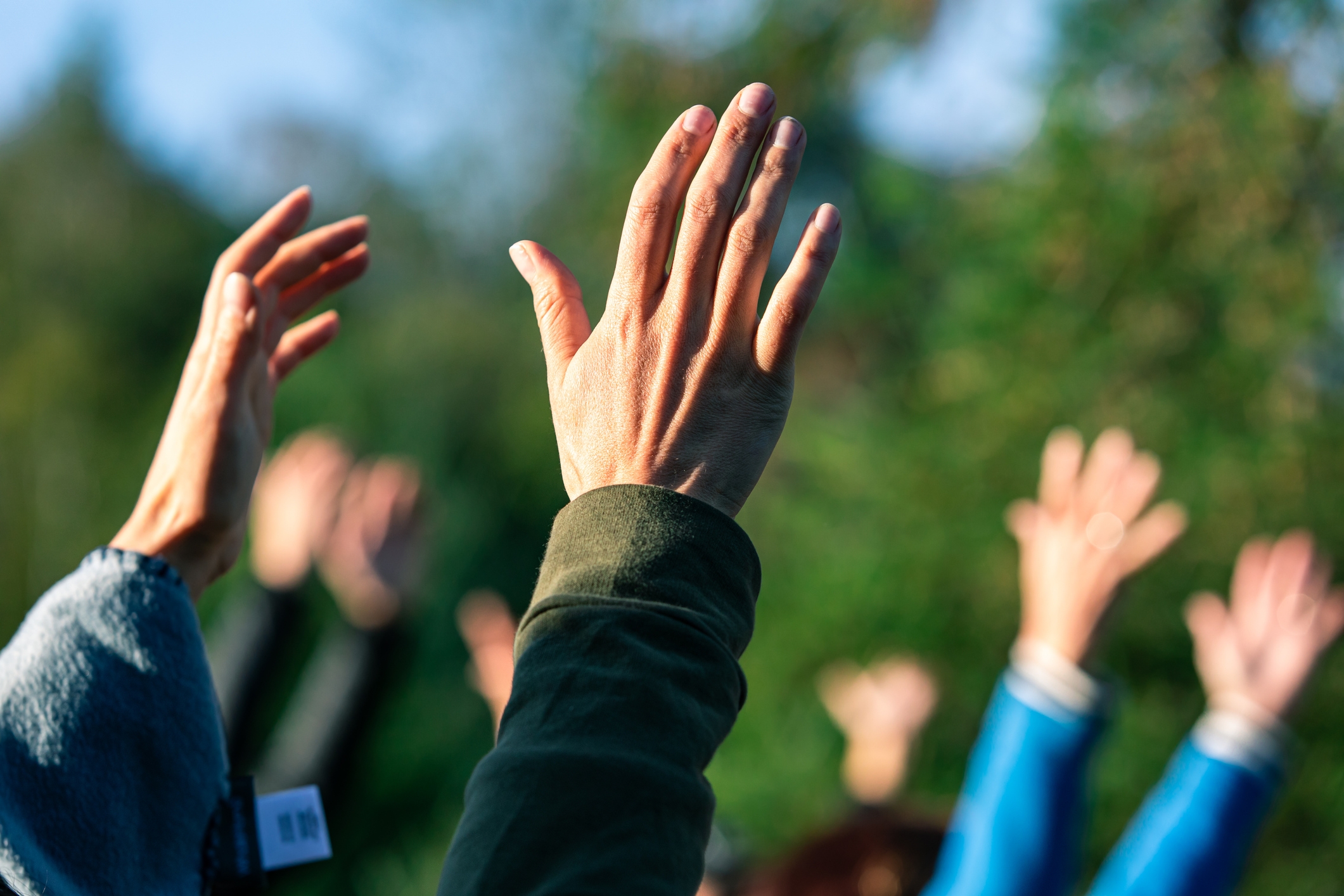 People raise their hands enthusiastically outdoors, possibly participating in an event or activity