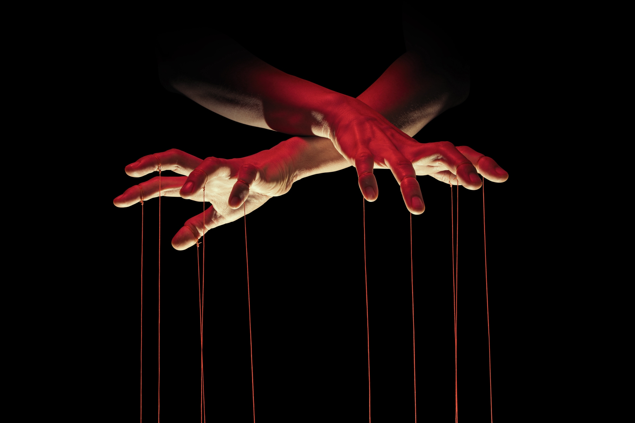 Hands holding puppet strings, creating a marionette effect against a dark background