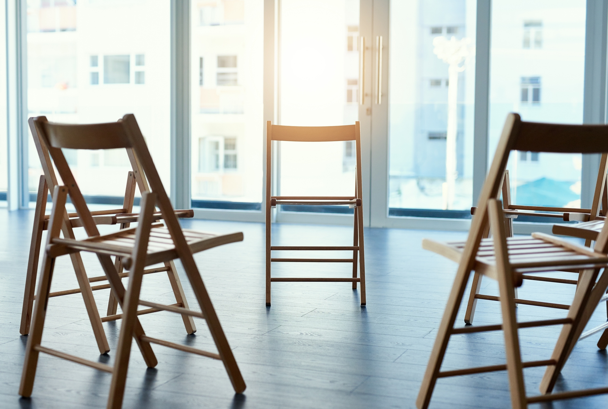 Wooden folding chairs arranged in a circle in a sunlit room, suggesting a meeting or group discussion setup