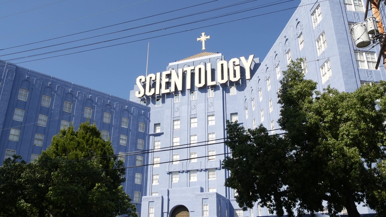 Scientology building with large sign on facade, featuring tall trees and power lines in foreground
