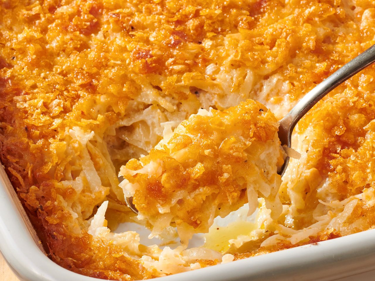 A person taking a scoop of Grandma's hash brown casserole from a pan.