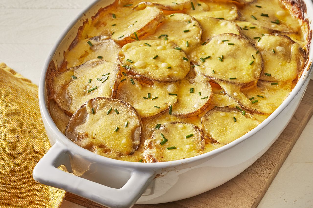 a close up view of creamy au gratin potatoes in a white oval casserole dish topped with fresh chives