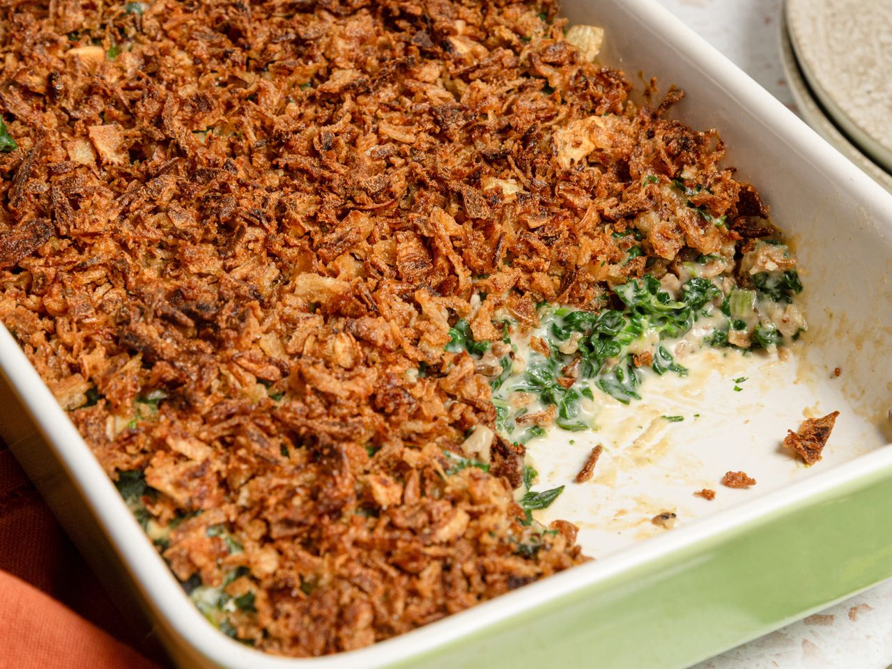 A spinach casserole topped with a crispy layer in a rectangular dish partially served showing the creamy spinach underneath