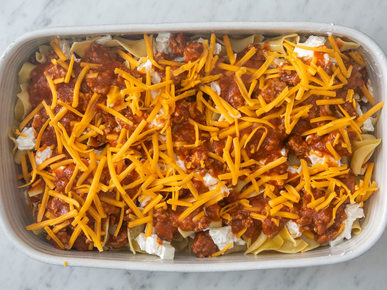 A baking dish containing layered ingredients including ground beef pasta cheese and sauce before baking