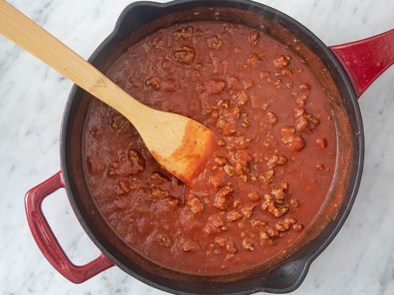 A stovetop pot containing ground beef and tomato sauce being stirred