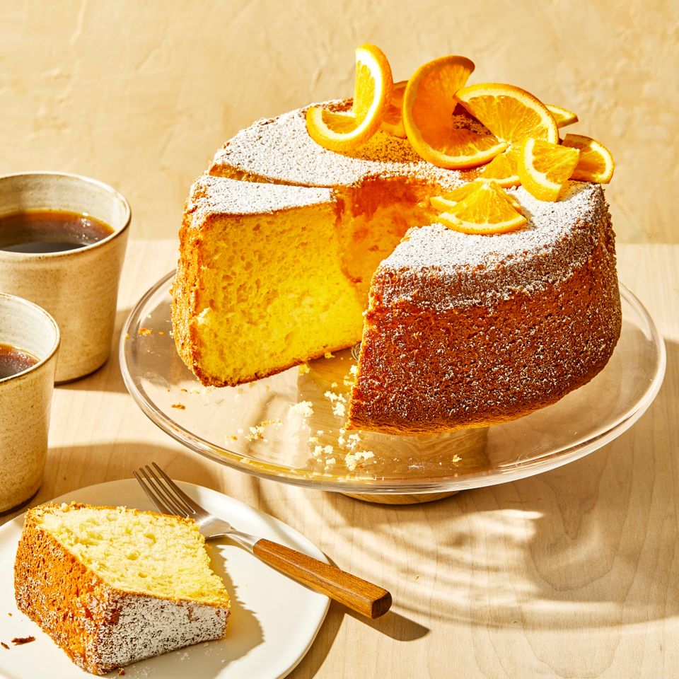 orange chiffon cake on cake stand with cups of coffee