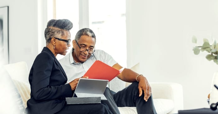 Two older adults discuss finances using a tablet on a couch.