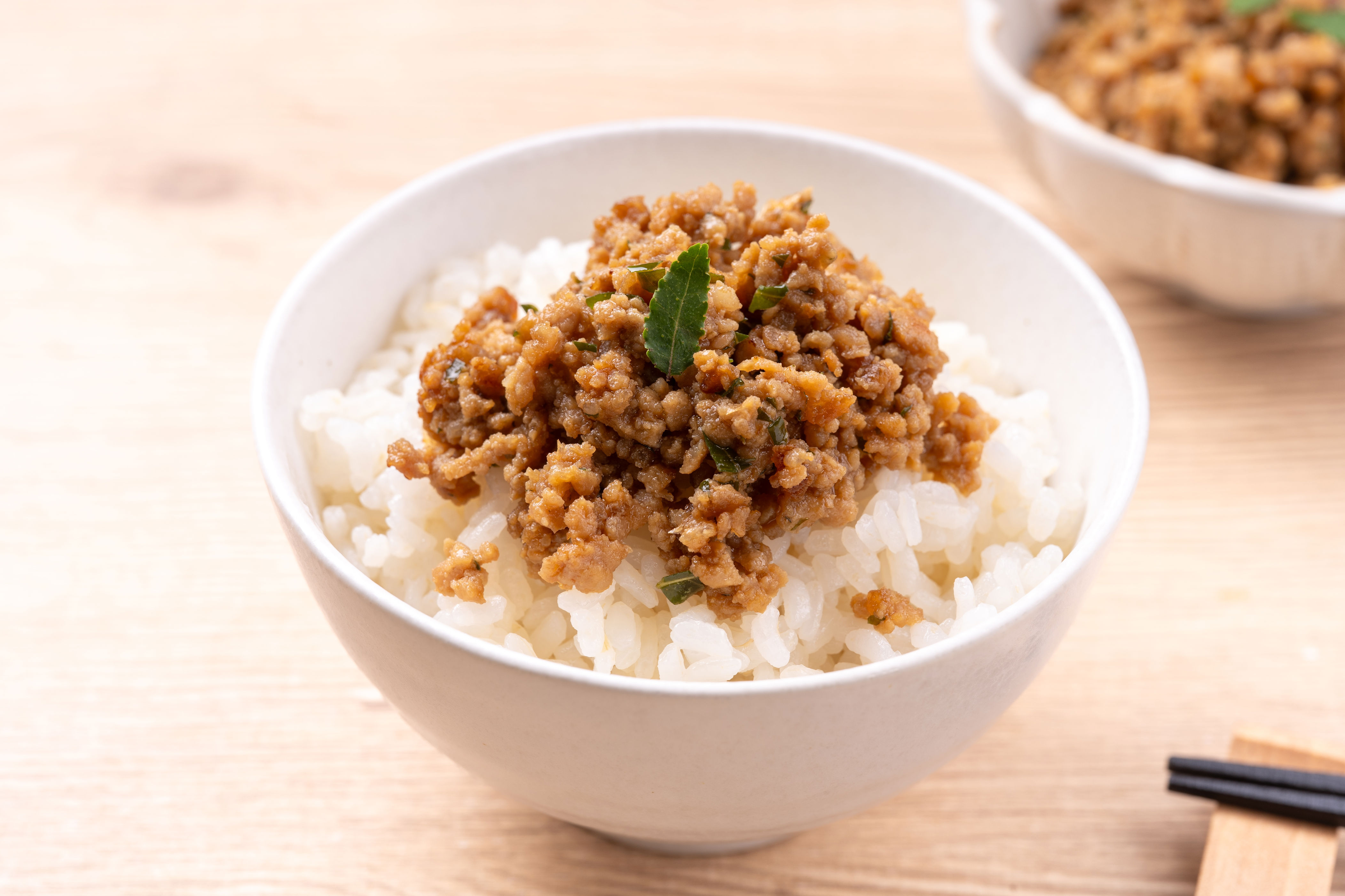 Bowl of rice topped with seasoned ground meat and herbs, with chopsticks on the side