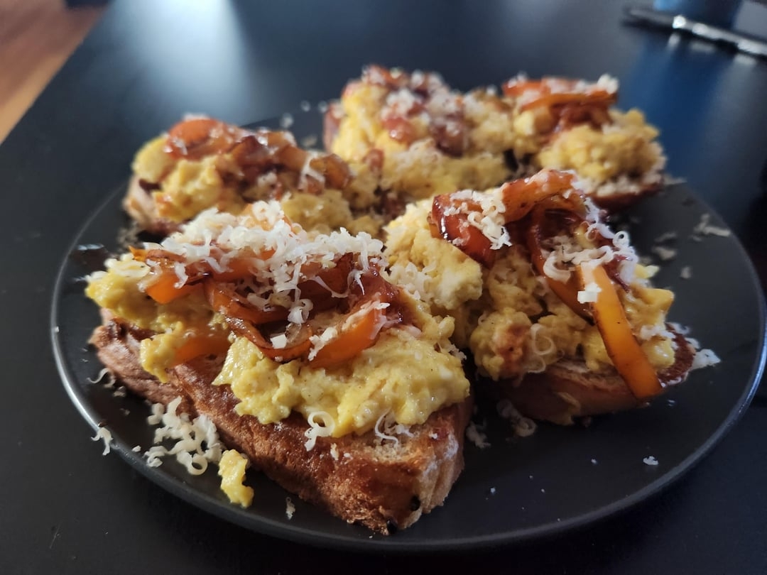 Plate of toast topped with scrambled eggs, sautéed onions, and grated cheese, set on a black surface