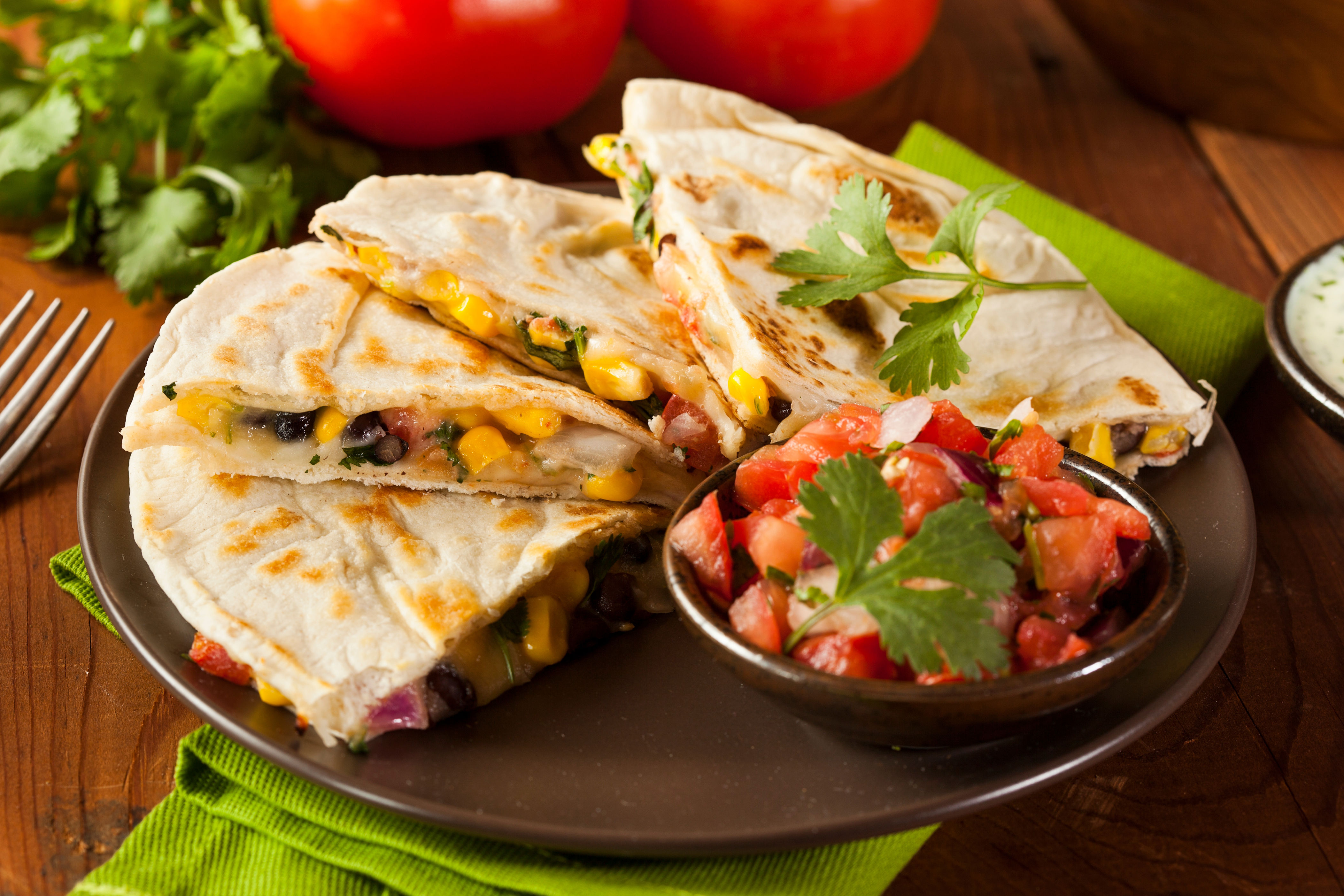 Quesadillas with cheese, corn, and beans on a plate, garnished with cilantro. Served with a side of fresh tomato salsa