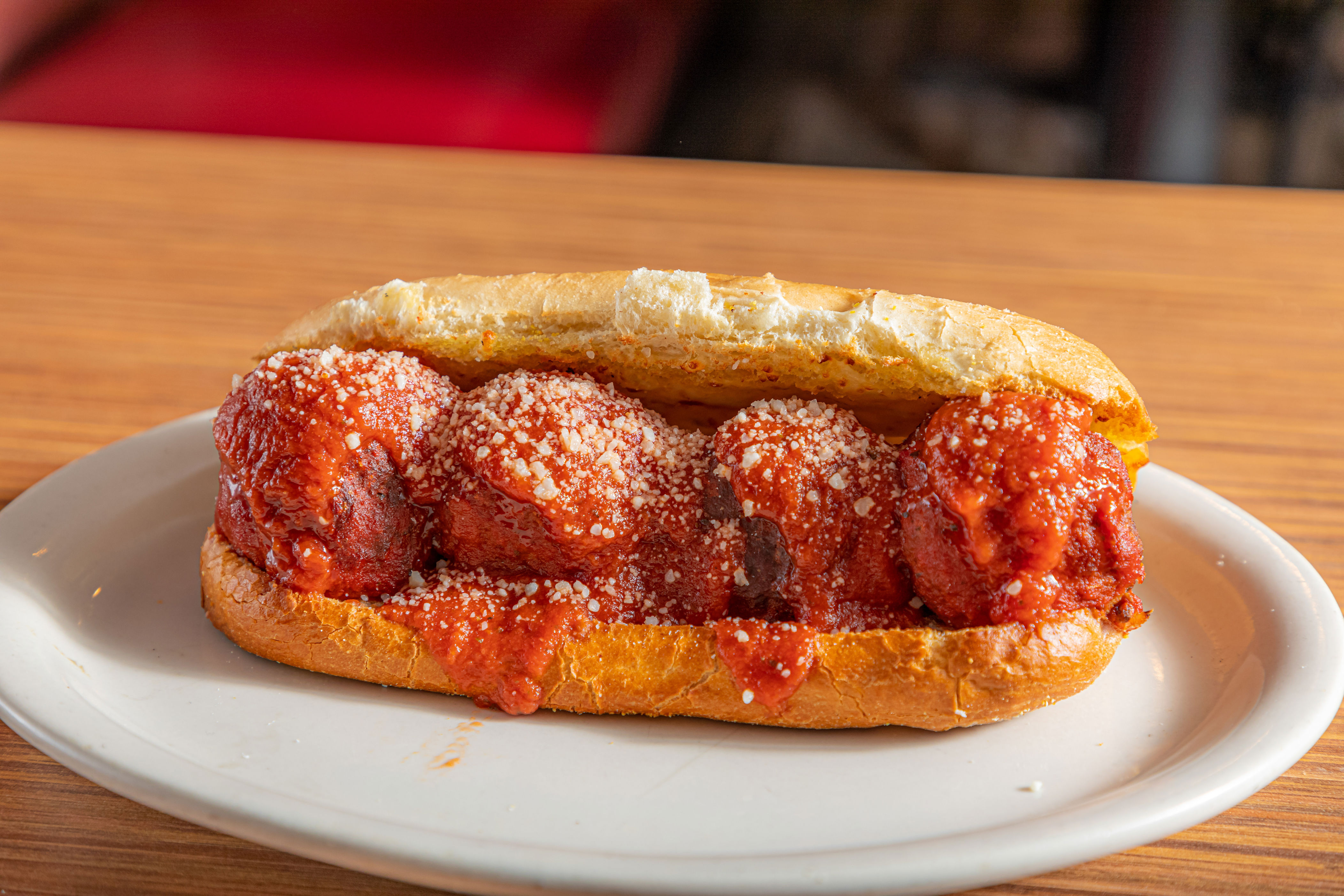 Meatball sub with marinara sauce and grated cheese on a white plate