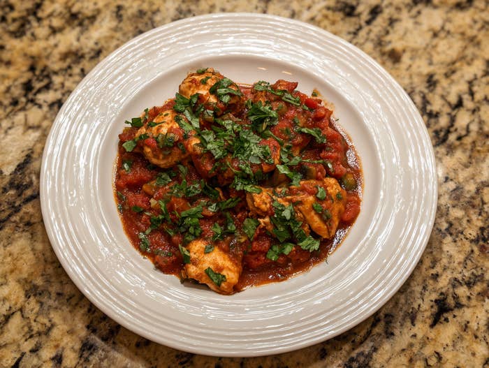 Plate of chicken meatballs in tomato sauce topped with fresh herbs on a stone countertop