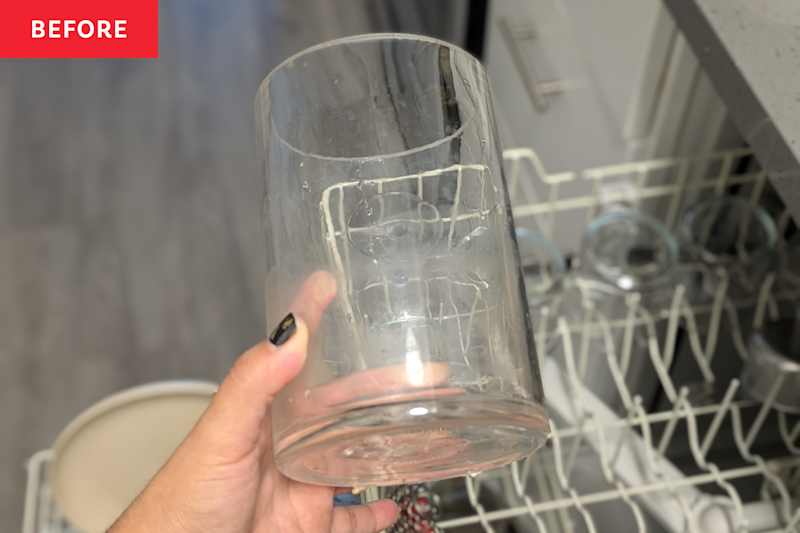 Someone holding glass jar over dishwasher before cleaning with vinegar.