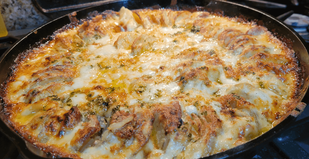 Cheese-covered sizzling dumplings in a skillet, topped with herbs, creating a savory and appetizing dish