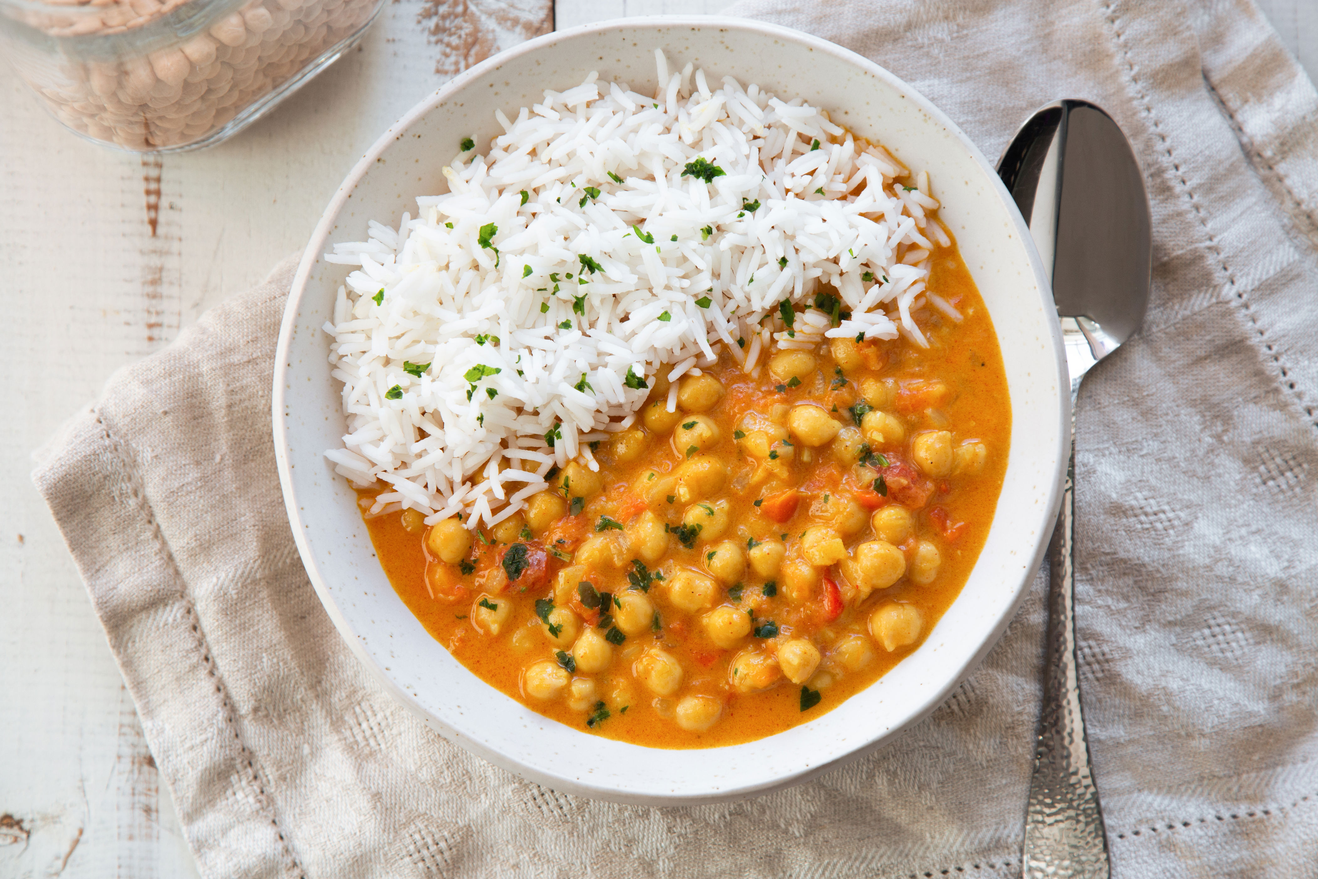 Bowl of chickpea curry with rice, garnished with herbs, served with a spoon on a cloth napkin