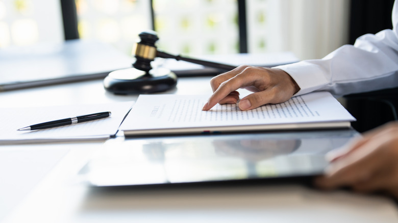 A person reading legal documents with a gavel beside on the desk.