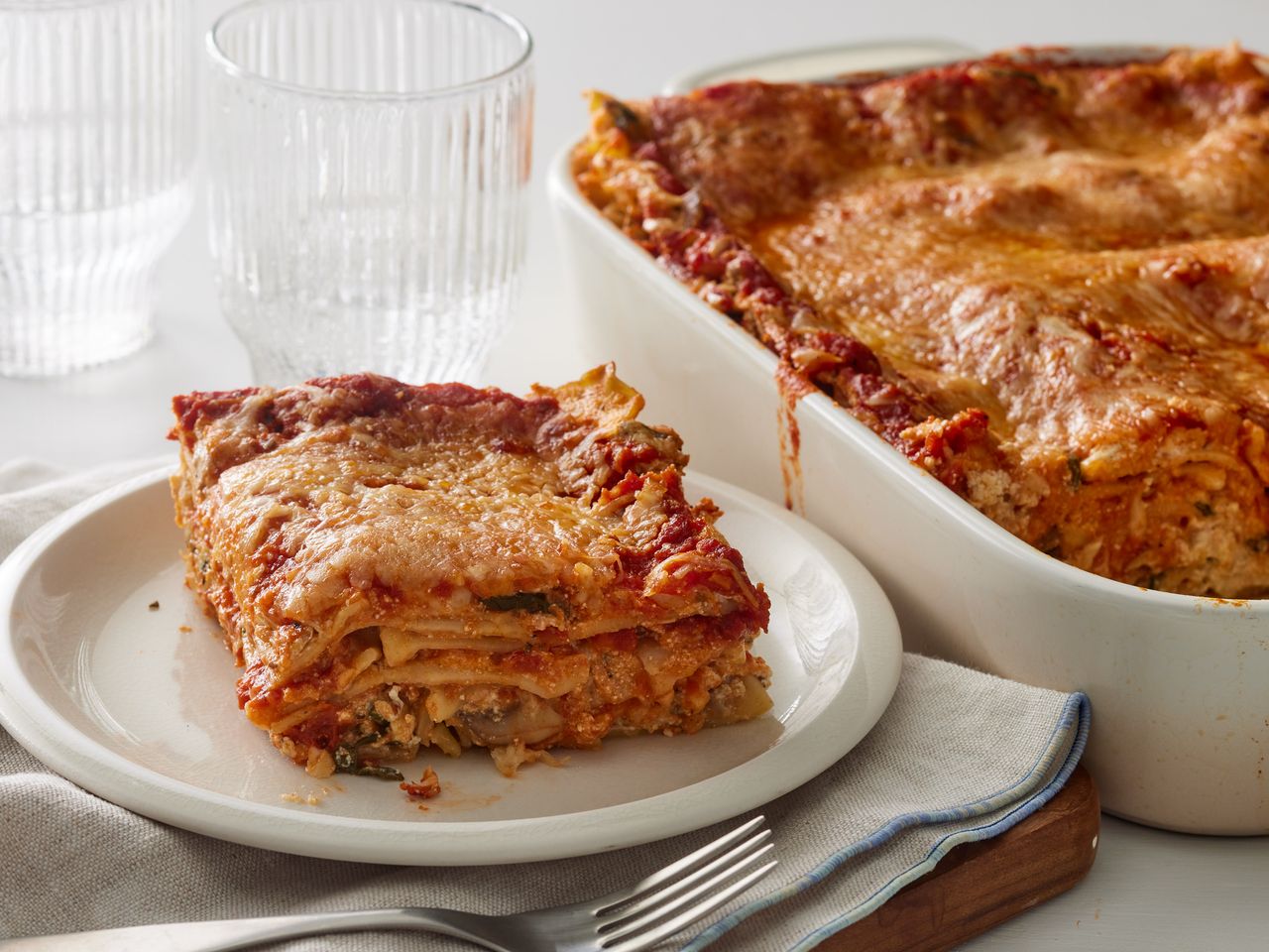 A plated slice of spinach lasagna, next to the baking dish of spinach lasagna