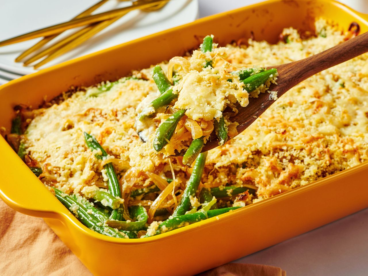 Green bean casserole in a yellow baking dish with a wooden spoon scooping a portion