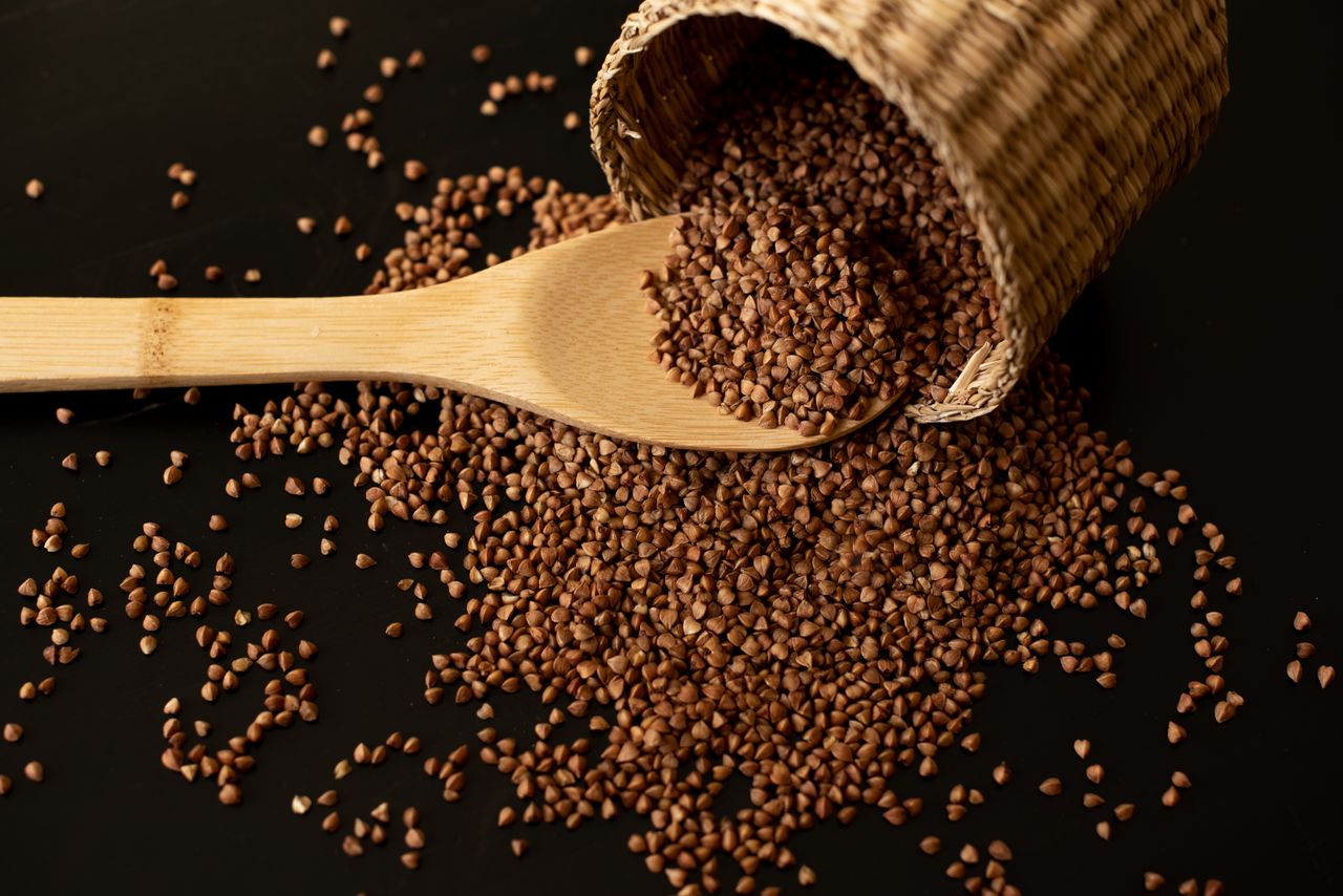 Buckwheat seeds in wooden spoon on a brown wooden table.