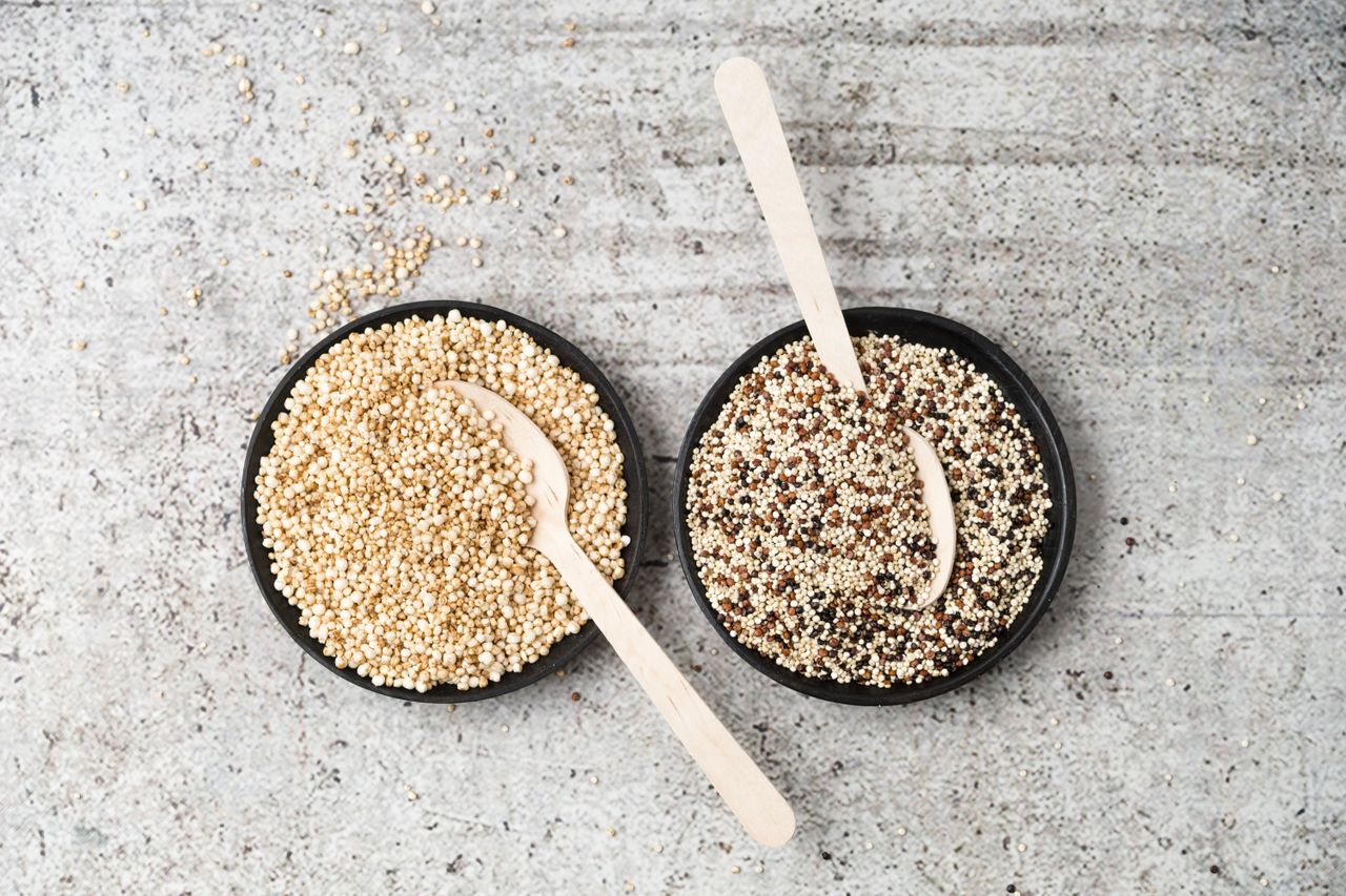 Two black bowls with wooden spoons filled with quinoa grains.