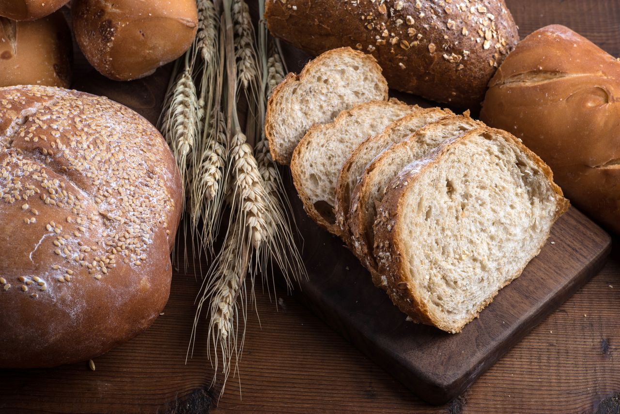 Slices and loaves of bread and wheat grains on a wooden cutting board