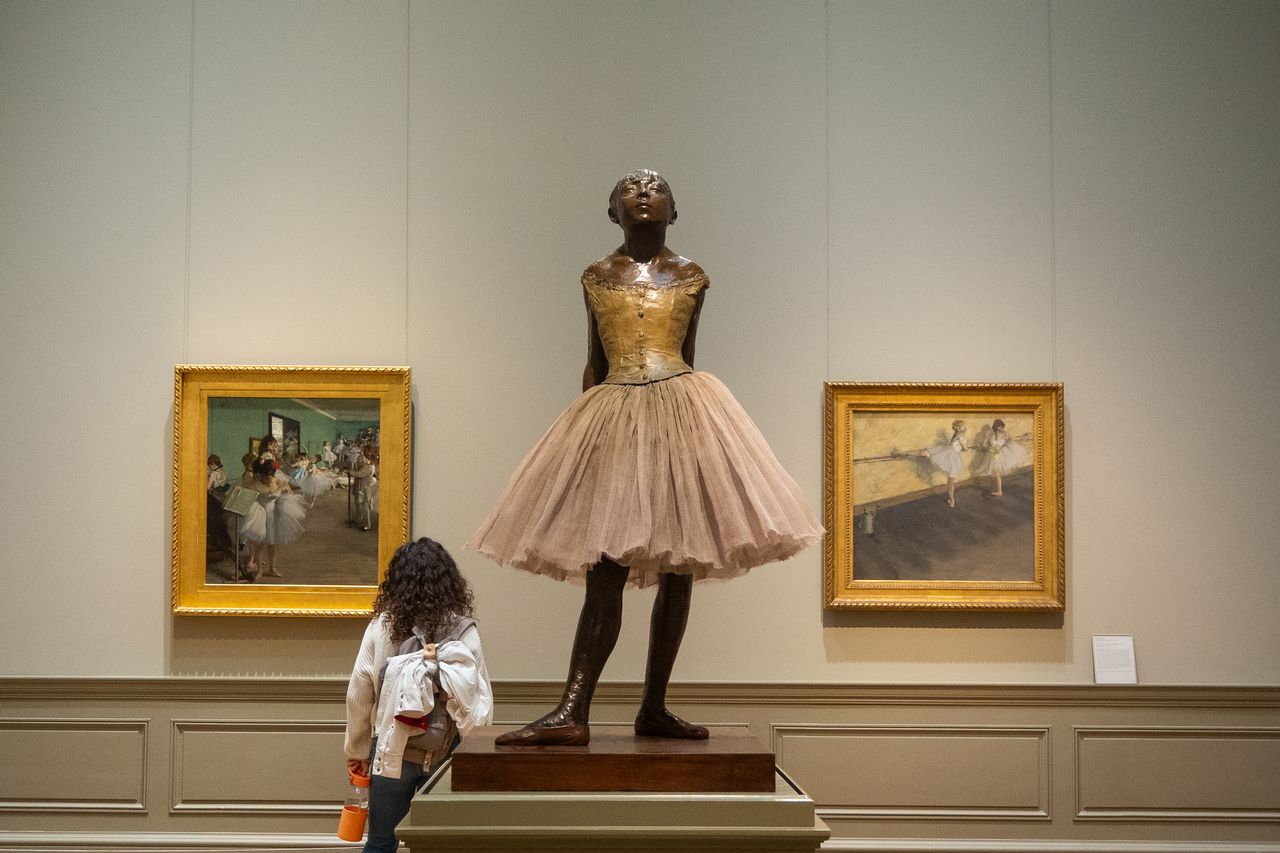 A woman looking at paintings next to a famous statue of a ballerina