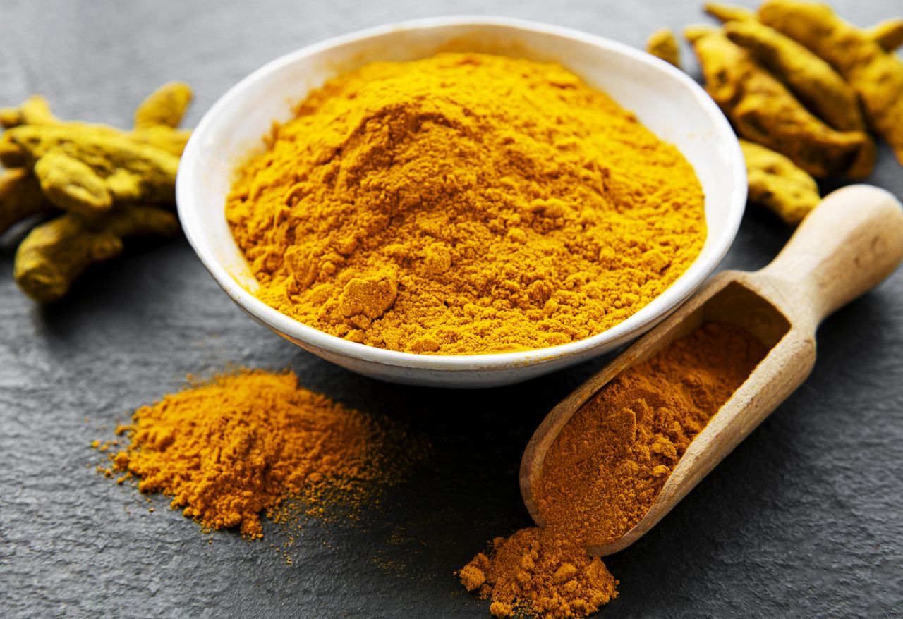 Bowl and scoop with turmeric powder and turmeric roots on a black background
