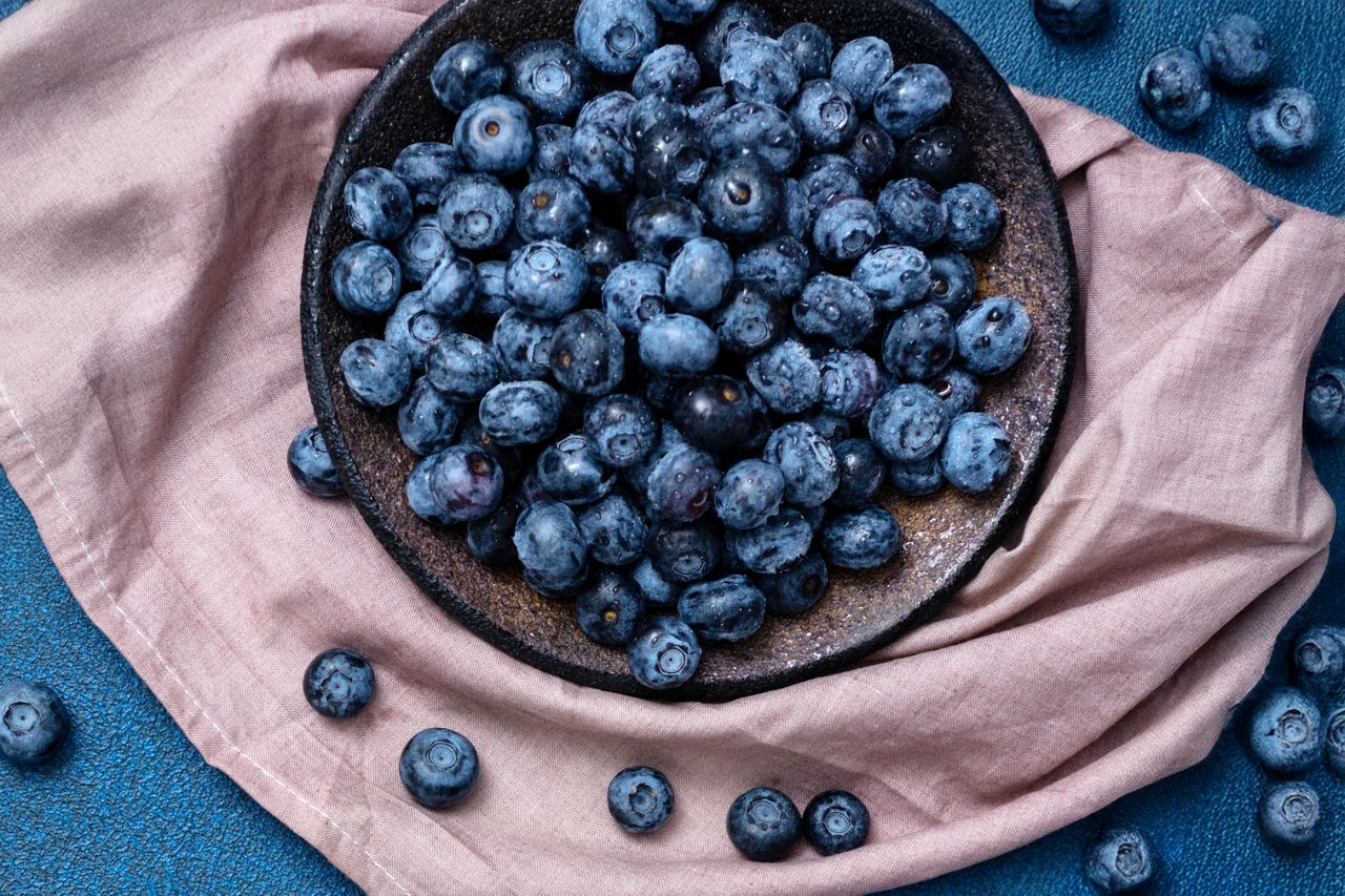 Plate with fresh blueberries on a blue background. Napkin with fresh berries. View from above. Focus on the plate.
