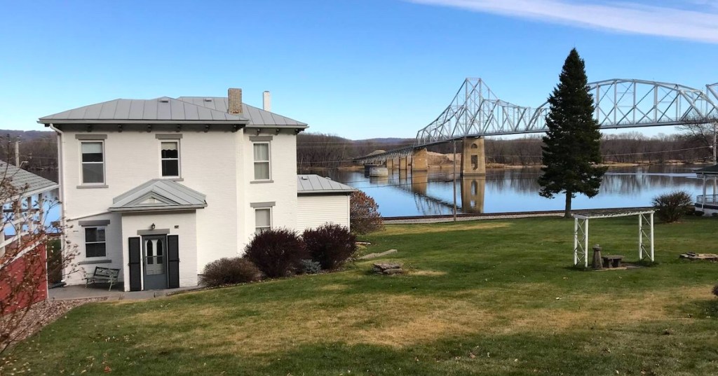 A white house sits on a green lawn overlooking the Mississippi River and the Black Hawk Bridge in Lansing, Iowa.
