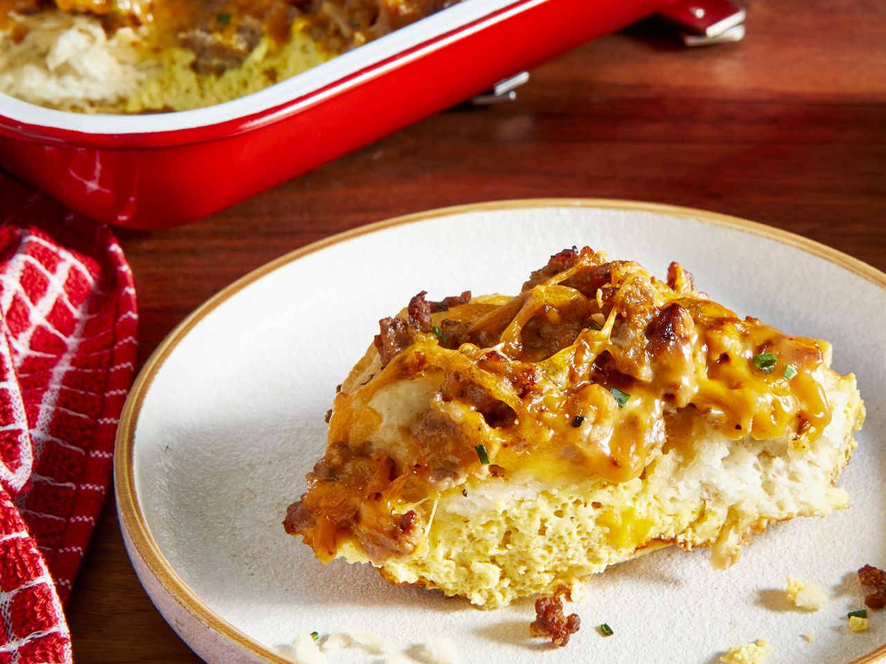 a serving of Biscuits and Gravy Casserole on a plate with a red baking dish of casserole in the background