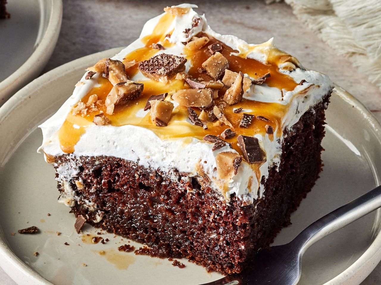 A slice of dessert cake topped with whipped cream caramel drizzle and crushed candy pieces served on a plate