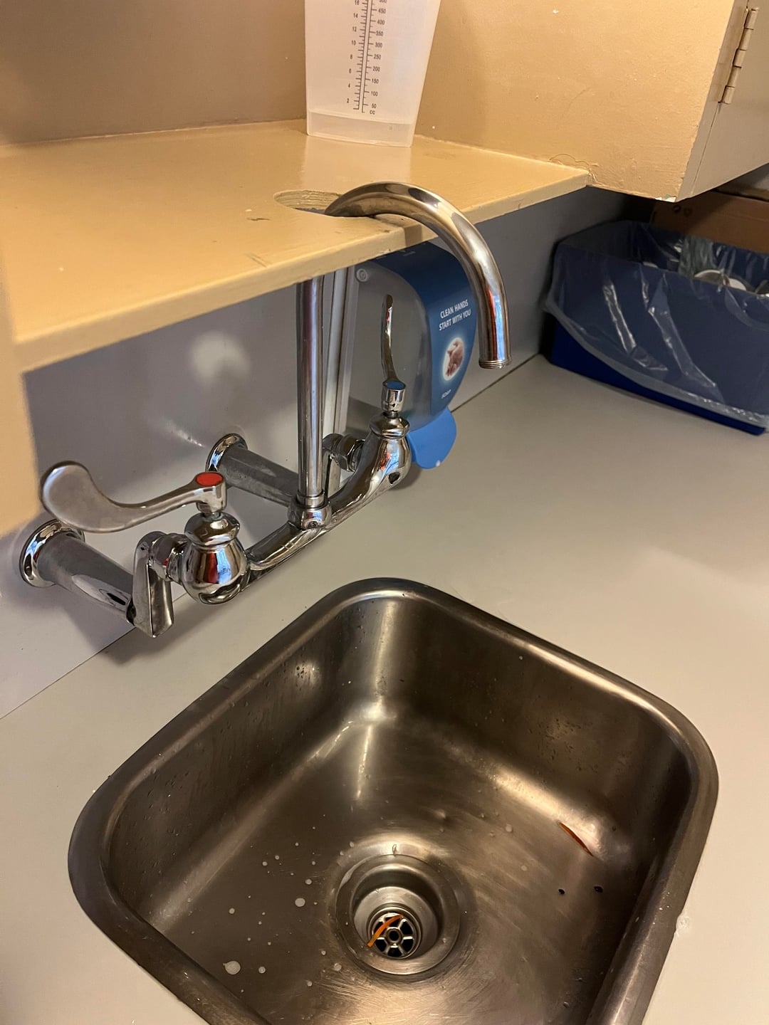 A kitchen sink with a tall, curved faucet and dual handles. A measuring cup sits on the counter above the faucet