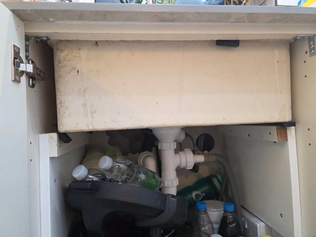 Under-sink cabinet filled with cleaning supplies, bottles, and bags