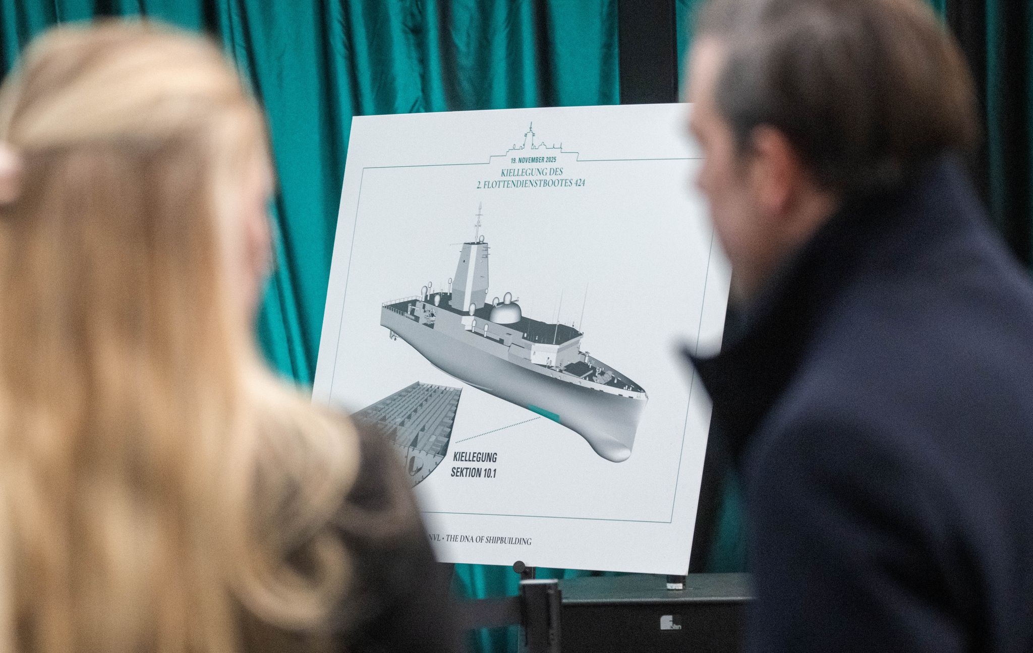 Gäste betrachten in der Werfthalle der Peene-Werft eine Zeichnung des neuen Flottendienstbootes.