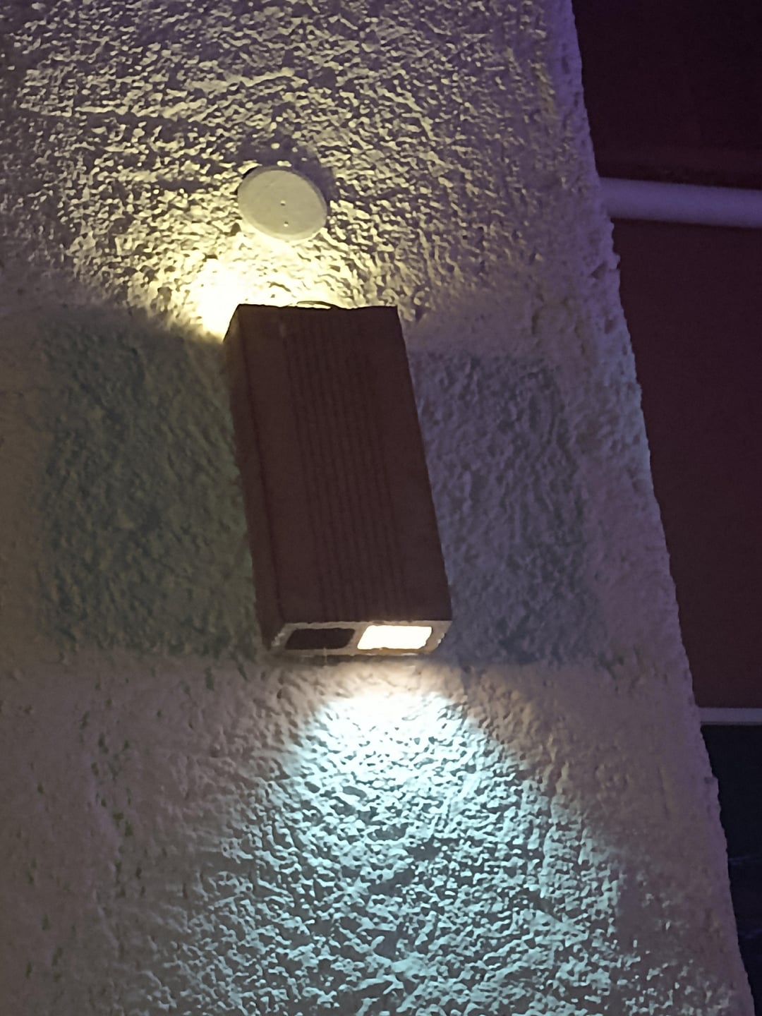 Wall-mounted outdoor light fixture illuminating a textured surface