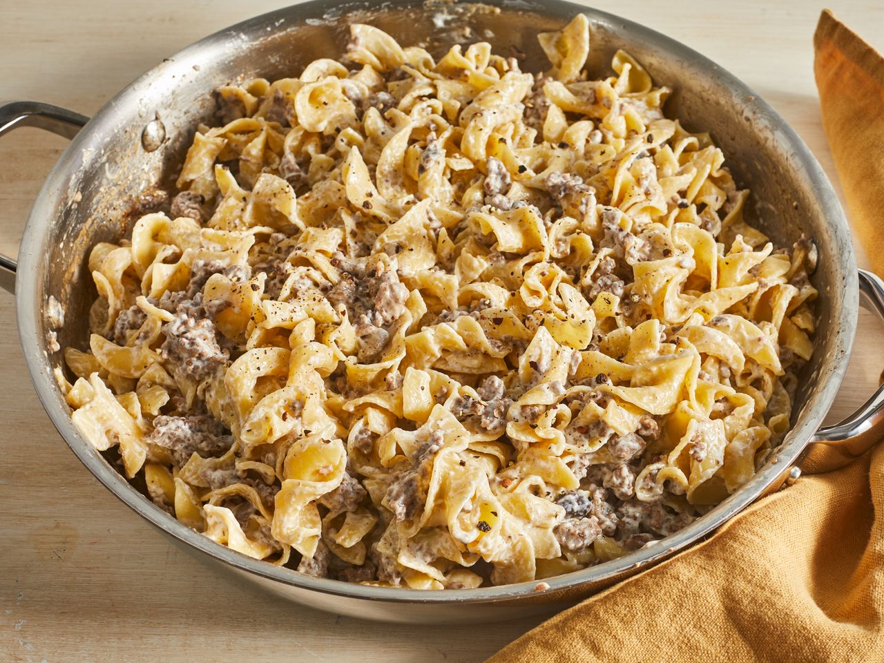 close up view of beef stroganoff in a pan, next to a kitchen towel