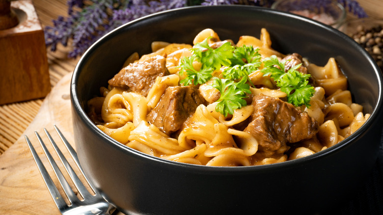 Beef and noodles with garnish served in a black bowl
