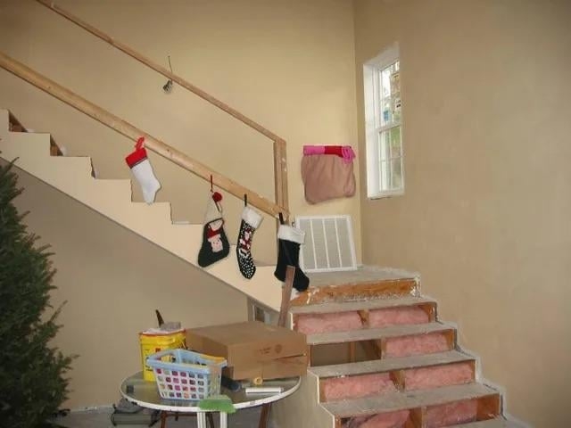 Unfinished staircase with makeshift Christmas stockings hanging on the railing. Construction materials are visible around the area